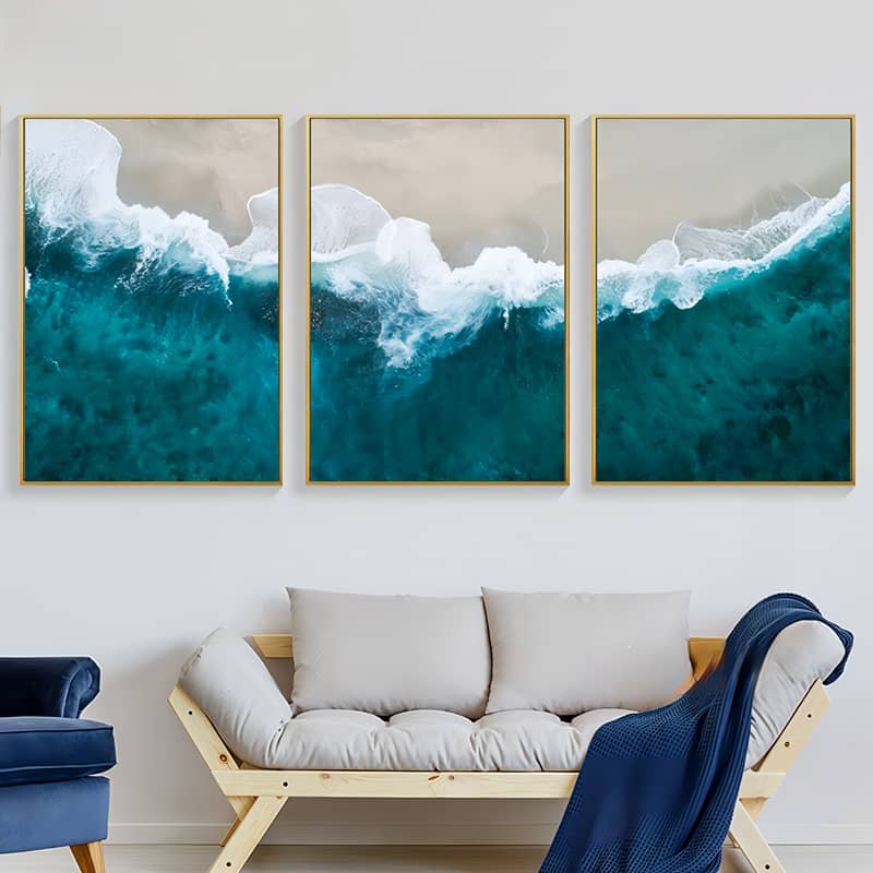 3-piece ocean wave art collection above a cozy couch with pillows and blanket in a modern living room.