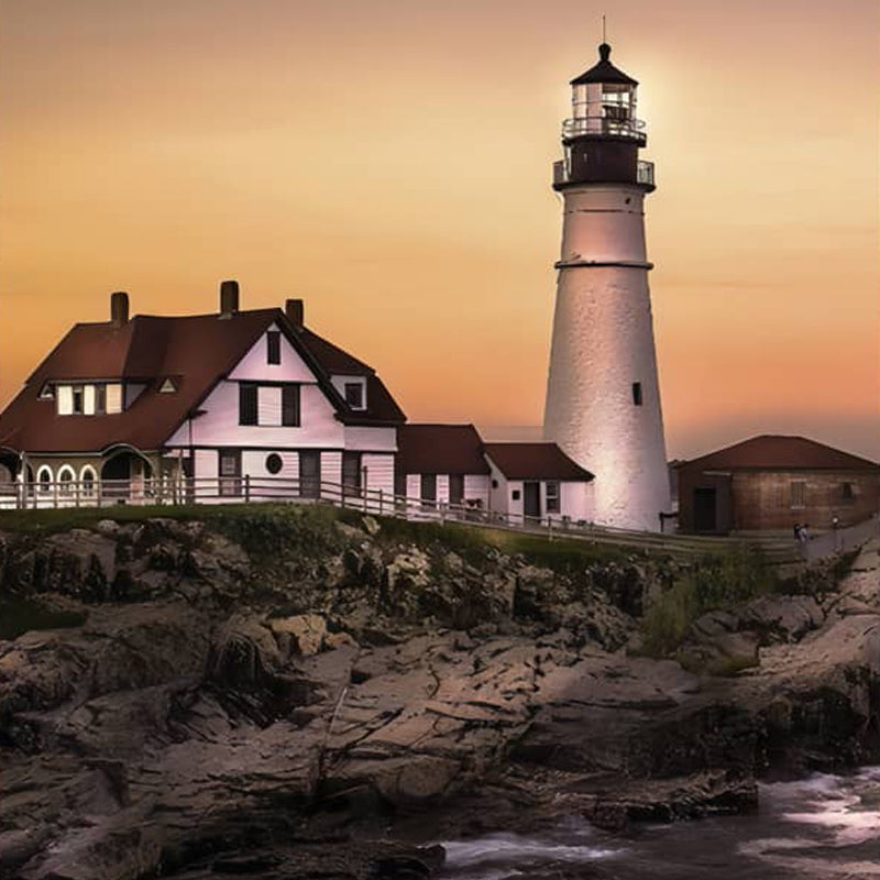 Lighthouse with attached house on rocky coast during sunset.