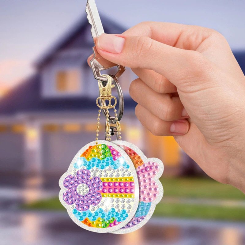 Hand holding a colorful, gem-encrusted keychain with a house in the background