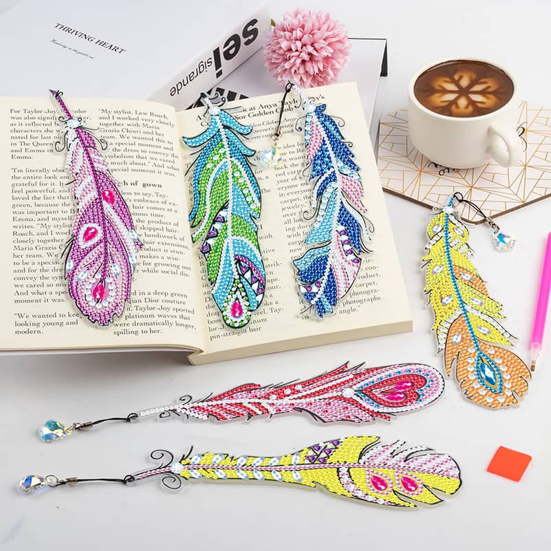 Diamond Painting Feather Bookmark 6-Pack displayed on open book next to coffee cup, showcasing colorful and sparkly designs.
