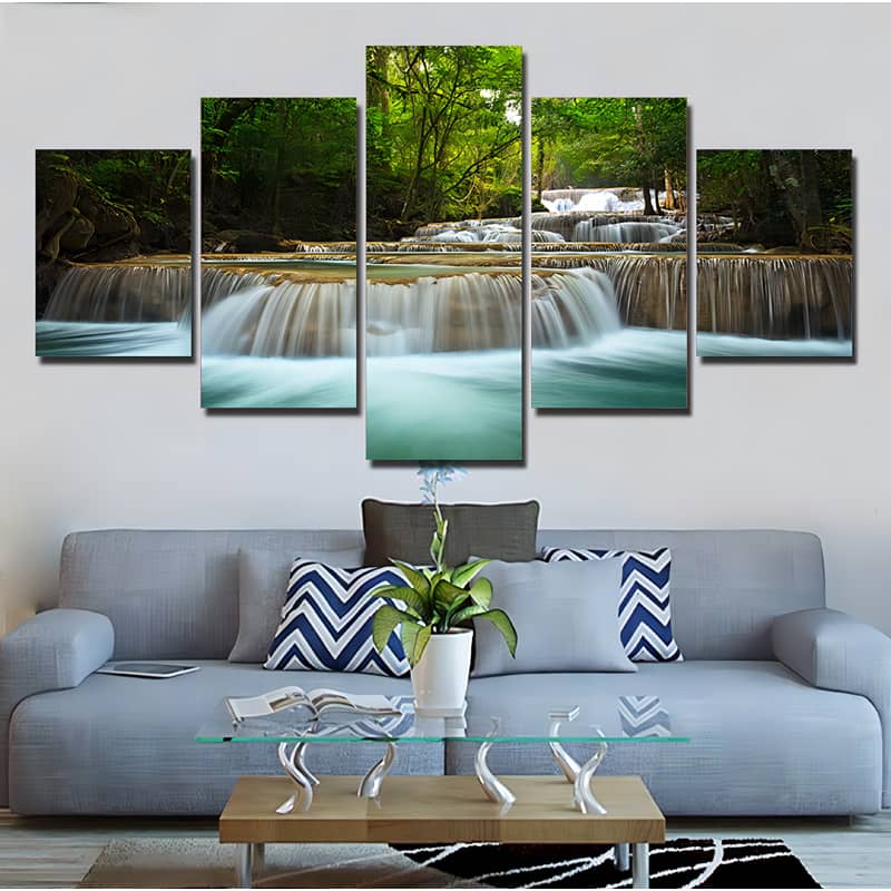 Diamond painting of a serene forest waterfall split into five panels, displayed above a modern living room sofa with decorative pillows.