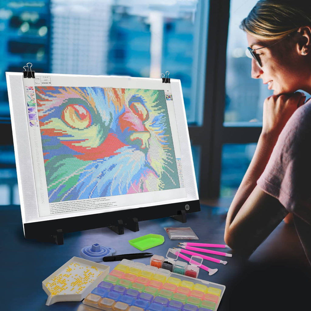 Person using Diamond Painting LED Light Pad to illuminate a colorful diamond painting project with tools and accessories.